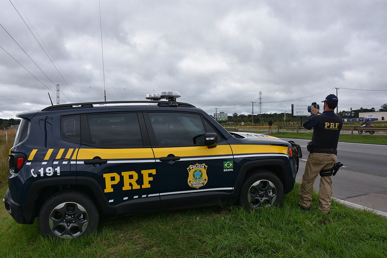 Viatura da PRF e agente com equipamento portatil em operacao de fiscalizacao em rodovia federal