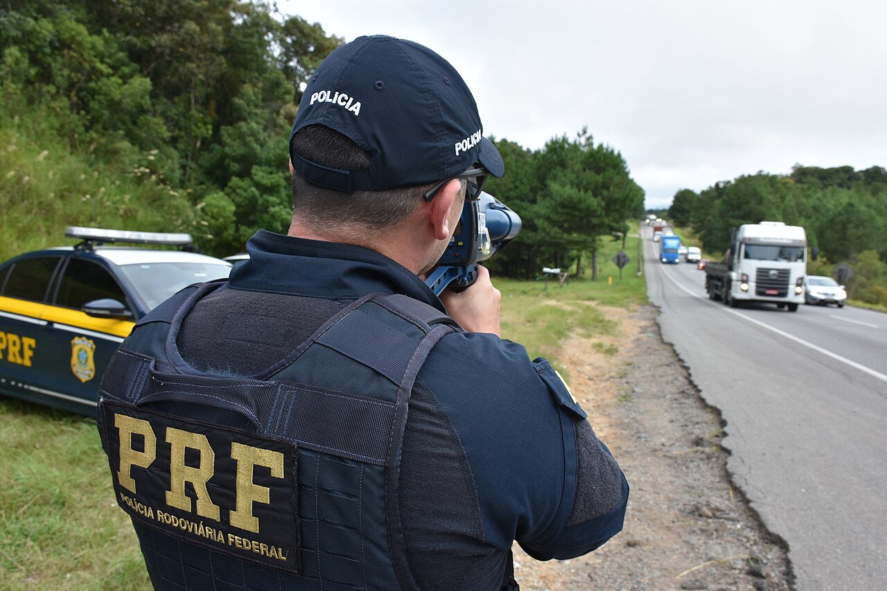 Agente da Policia Rodoviaria Federal fiscalizando caminhao de carga em rodovia federal